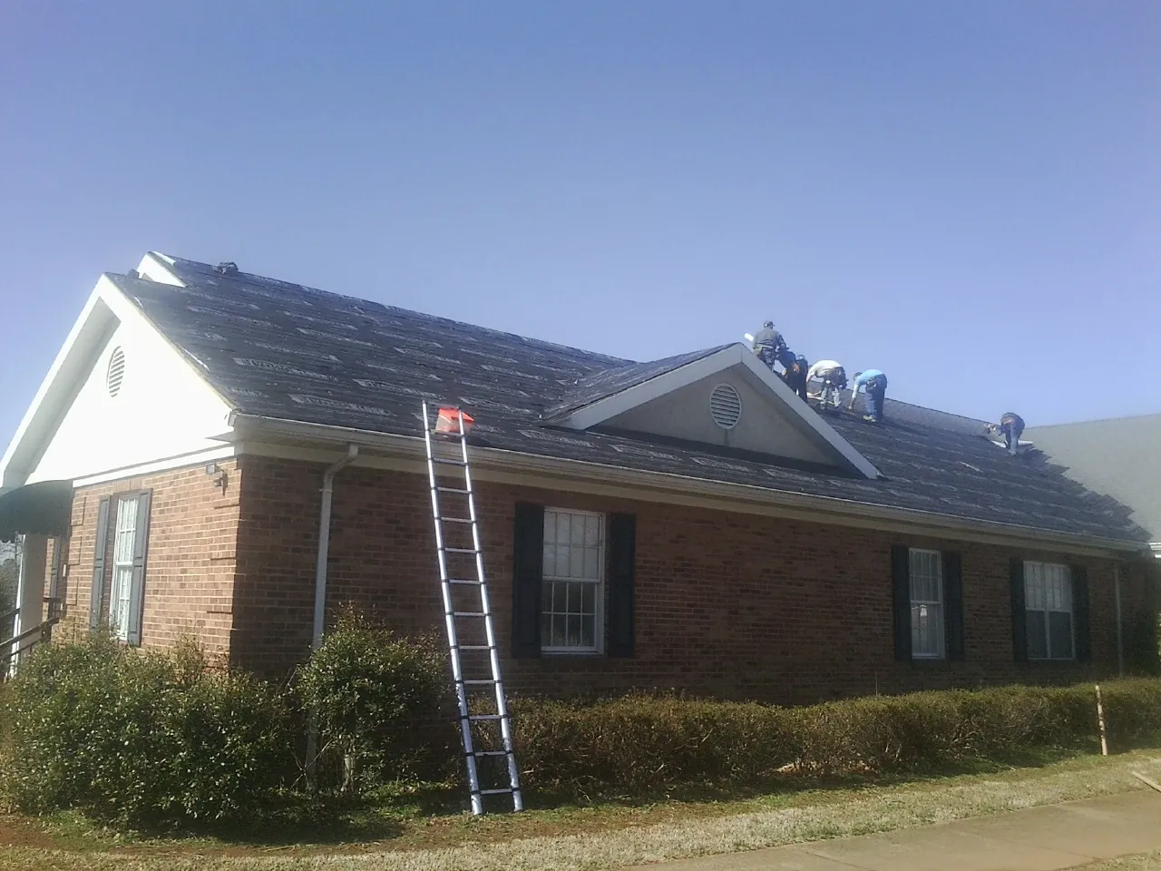 Crew tearing shingles off a brick ranch roof with a ladder set — Metal Roof Repair work by our crew in Menan