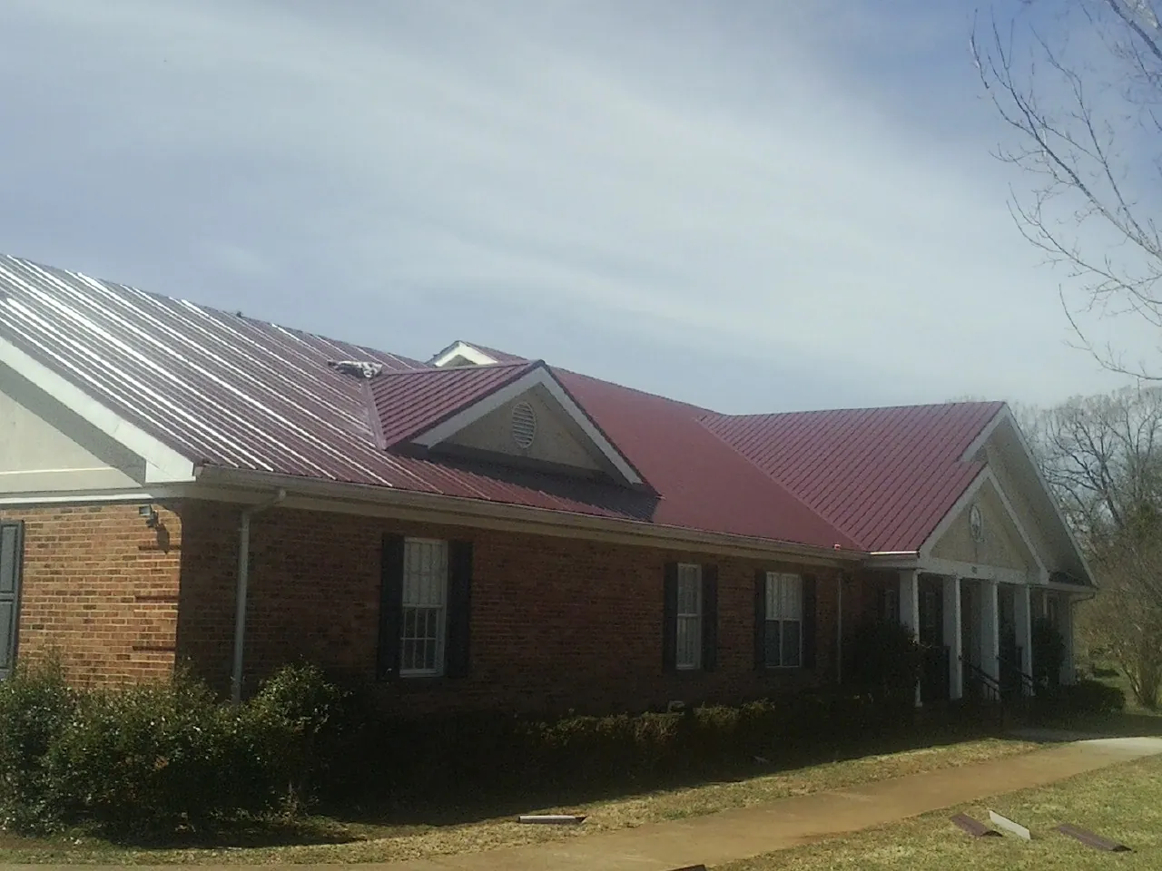 Red metal roof with gabled entries on a long brick building, from a Hail Damage Roof Repair job in Menan