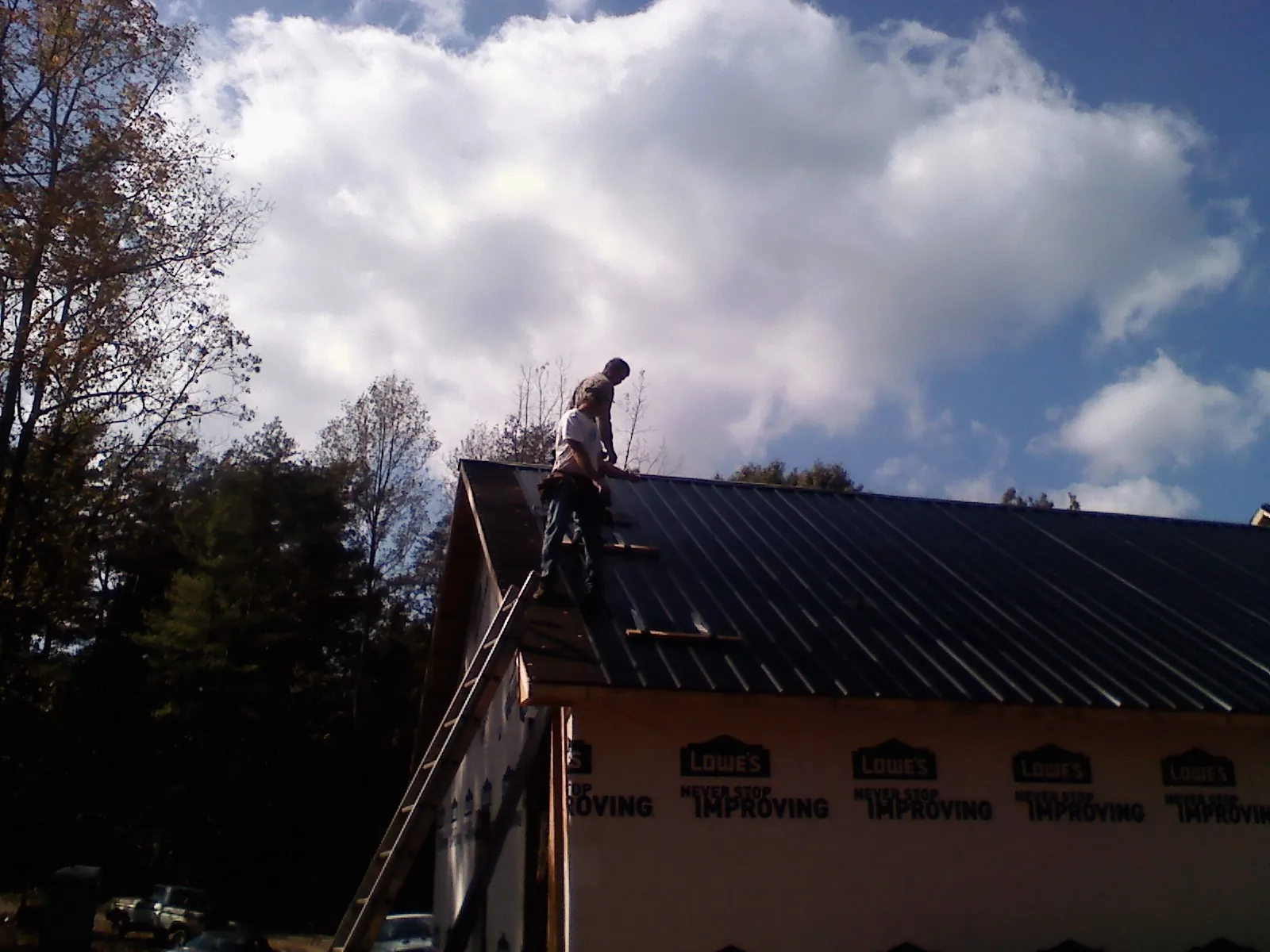 Roofer fastening dark metal panels high against a cloudy sky, from a Roof Inspection job in Menan