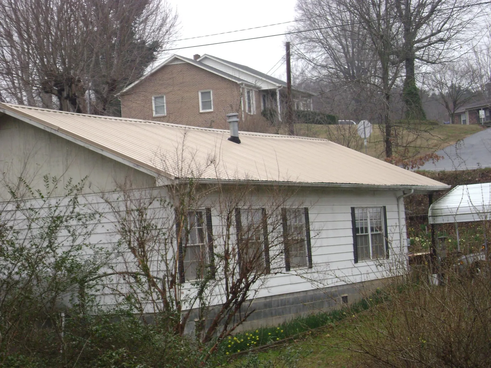 Tan metal roof on a white sided house set into a hillside — Commercial Roofing by Roofing Brothers in Menan